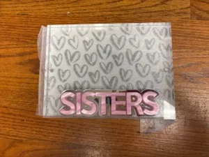 Pink SISTERS sign on heart-patterned card